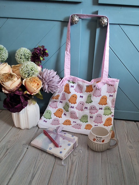 A white fabric tote shopping bag with pink gingham handles and bows and a repeating pattern of cute pastel ghosts, 