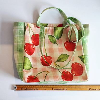 Tote bag covered in cherries and green cherries. Flay front view with measuring stick
